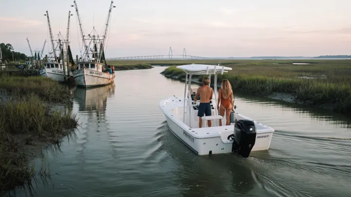A centre console boat idling down the creek past shrimp boats