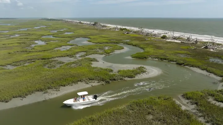 Aerial over tidal creeks in green marsh with a small boat running north